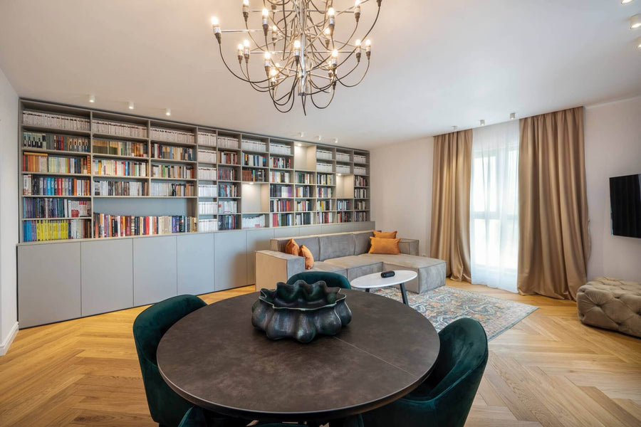 Herringbone wood floor in a living room with wall to wall book shelves and large table in the middle.