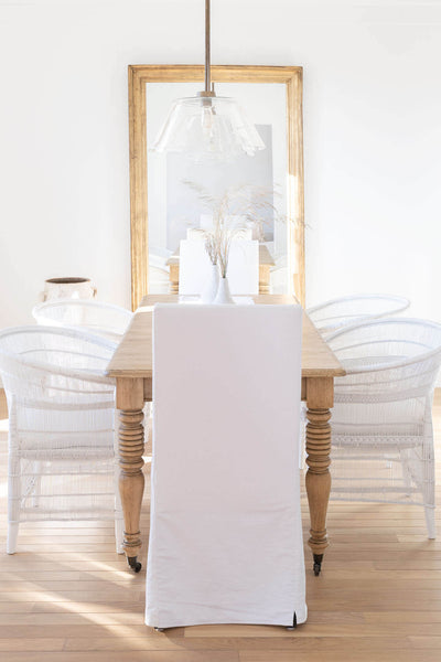 Natural wood dining table with white chairs and decor placed in front of a mirror