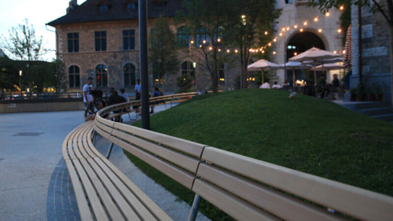 Close up image of wood benches curving around a lawn at night.