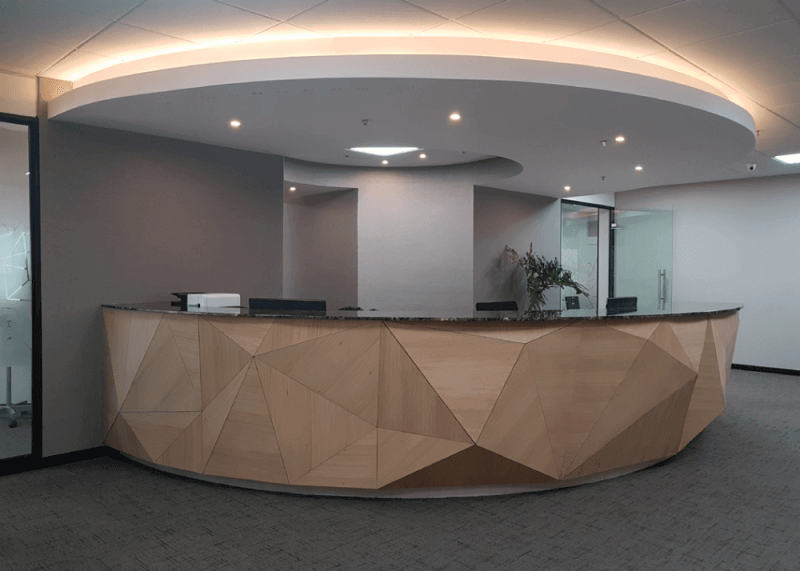 A curved reception desk with geometric wood shapes extruding from the front.