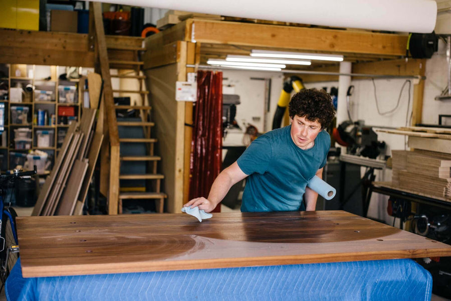 Man applying hardwax oil wood finish to a walnut table top.