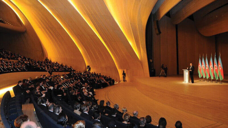 An audience watching a speaker in a large wood auditorium.