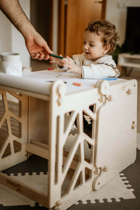 A child is given a marker to color with while sitting at a toddler learning tower transformed into an art table.