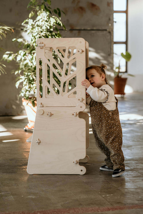 A child peaks behind a toddler learning table, curious about the intricate geometric design.