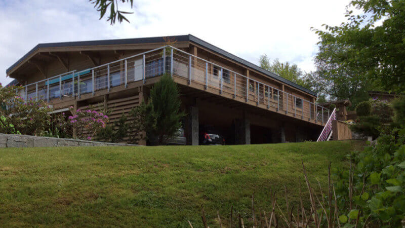 A renovated chalet with a wood balcony overlooks a green yard.