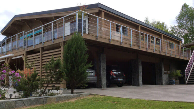 A restored wood cabin with a balcony around the upper level and a carport underneath the upper level.