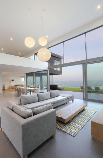 Living area of a modern house with glass windows and walls, modern decor, and a view of the ocean.
