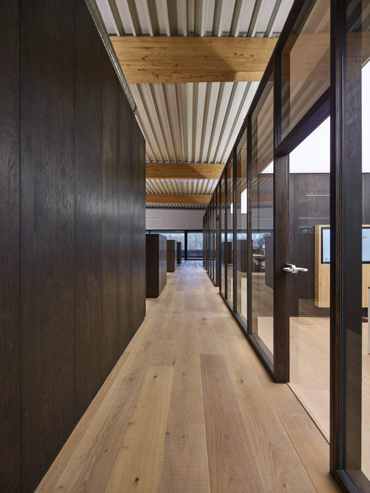 A hallway with wood floors, wood wall panels and glass office barriers at the Rubio Monocoat headquarters.