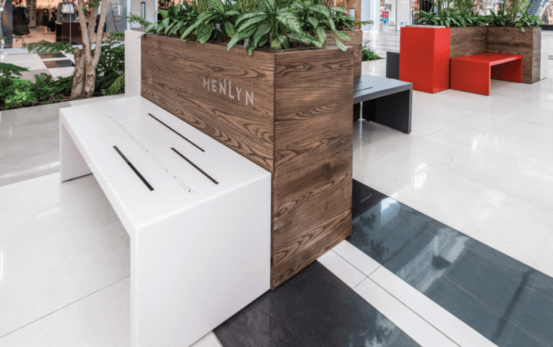 A wooden planter box with a dark matte finish and a white benchs eat pressed against it.